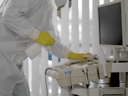 Medical Worker In Ppe Doing Sanitization Of Equipment In Hospital Room